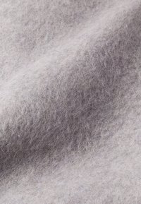 Tessuto in feltro grigio chiaro con una superficie morbida e testurizzata, caratterizzato da un aspetto leggermente peloso e una distribuzione del colore uniforme.