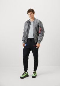 Grå bomberjakke med lynlås-lomme, grå t-shirt, sorte joggers med Nike-logo og grønne træningssko med sorte detaljer.