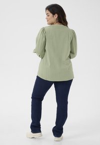 Ljusgrön texturerad blus med puffärmar, matchad med mörkblå jeans och vita sneakers. Synlig ribbad struktur på blusen.