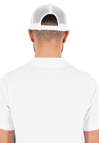 Camisa polo blanca con una textura suave, que presenta un collar clásico y un reverso liso. La gorra tiene un diseño de malla en blanco, con un borde plano.