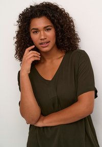 Top verde oliva a V con maniche corte, tessuto testurizzato e un sottile dettaglio della cucitura frontale, indossato da un modello con capelli ricci.