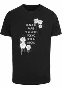 Melna t-krekls ar baltām ziedu grafikām, kurās ir rozes un pilsētu nosaukumi: Londona, Parīze, Ņujorka, Tokija, Berlīne, Seula. Vienkāršs, ikdienišķs dizains.