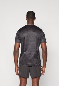Zwarte sport T-shirt met een subtiele lineaire textuur, korte mouwen, ronde hals en gecombineerd met donkere shorts.