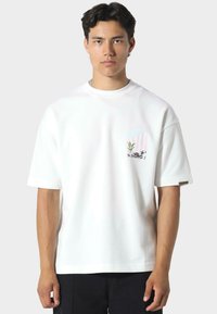 Valkoinen puuvillatee paita lyhyillä hihoilla, jossa on palmupuun ja raidallisen kuvion taskusuunnittelu. Rentoa istuvuutta, jossa on lievää tekstuuria.