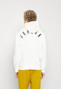 Felpa bianca con cappuccio, con la scritta curva "JORDAN" nera sul retro. Presenta polsini e orlo a costine, realizzata in un tessuto morbido.