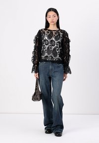 Schwarze Spitzenbluse mit Paisleymuster und Rüschenschultern, kombiniert mit dunkelblauen Schlagjeans und einer kleinen braunen Handtasche.