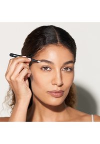 Pince à épiler noire avec une prise texturée tenue par une personne en train de façonner son sourcil. L'arrière-plan est d'une couleur neutre, mettant en valeur les outils utilisés.