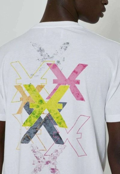T-shirt bianco in cotone con una stampa grafica colorata sul retro, caratterizzata da forme astratte sovrapposte nei colori rosa, giallo, grigio e verde.