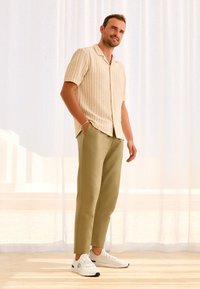 Hellbeige Kurzarmpullover mit vertikalen Streifen, kombiniert mit olivgrünen Hosen und weißen Sneakern. Weicher Stoff, lässige Passform.