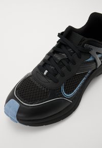 Zwarte sneaker met een gestructureerde mesh bovenwerk, contrasterende blauwe accenten, platte veters en een gevoerde zool. Heeft een gestroomlijnd ontwerp.