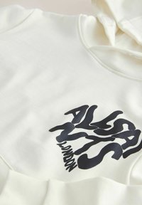 Sweat-shirt à capuche couleur blanc cassé avec l'inscription "ALSA 1776 LONDON" en grandes lettres noires ondulées sur la poitrine.