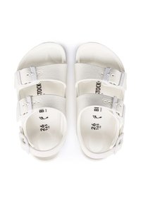 Białe sandały z dwiema regulowanymi paseczkami, wykonane z gładkiego materiału, z metalowymi klamrami i wydrukowanymi szczegółami rozmiaru na wkładce.