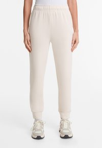 Light beige sweatpants made of soft fabric, featuring an elastic waist, tapered legs, ribbed cuffs, and no visible logos or embellishments.