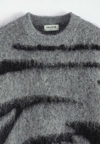 Pull gris flou avec des motifs abstraits noirs et une étiquette blanche à l'intérieur du col portant l'inscription "FRILIVIN TAILLE M".