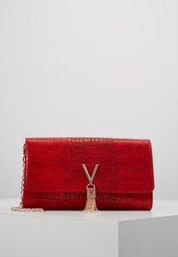 Borsa in finta pelle di coccodrillo rossa con un pompon in tono oro, caratterizzata da un accentuazione metallica a forma di V e una tracolla a catena.