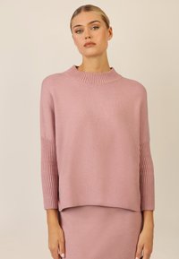 Rosa gestrickter Pullover mit einem gerippten Rollkragen und langen Ärmeln. Weiche Textur mit einer lockeren Passform, kombiniert mit einem passenden Rock.
