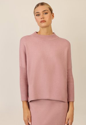 Pink knitted sweater with a ribbed turtleneck and long sleeves. Smooth texture with a relaxed fit, paired with a matching skirt.