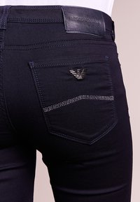 Marinblå denimjeans med en figursydd design, med en läderpatch i midjan och en detalj i guldfärg på bakfickan.