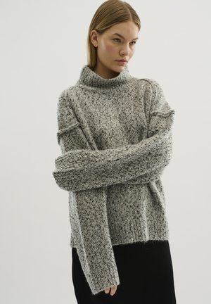 Maglione grigio a collo alto con un motivo testurizzato, vestibilità oversize e spalle scese. Il tessuto sembra morbido e accogliente, con maniche lunghe.