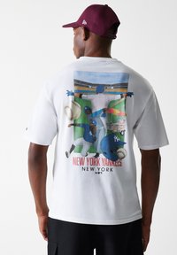 Camiseta blanca de algodón con un gráfico de béisbol colorido en la espalda, que muestra jugadores y una pelota de béisbol, con el texto "NEW YORK YANKEES".