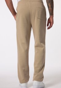 Bežové bavlněné tepláky s elastickým pasem, zadní kapsou a zúženými nohavicemi, doplněné bílými sportovními botami.