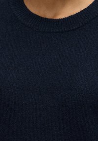 Gros plan d'une personne portant un pull en maille côtelée bleu marine foncé avec un col rond.