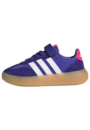 Μωβ αθλητικό παπούτσι Adidas με λευκές ρίγες, σόλα από καουτσούκ, κορδόνια με επιπλέον λουράκι με βέλκρο και ροζ ταμπελάκι στη φτέρνα.