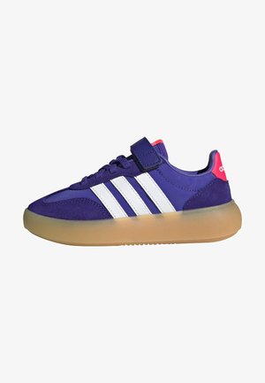 Μωβ αθλητικό παπούτσι Adidas με λευκές ρίγες, σόλα από καουτσούκ, κορδόνια με επιπλέον λουράκι με βέλκρο και ροζ ταμπελάκι στη φτέρνα.