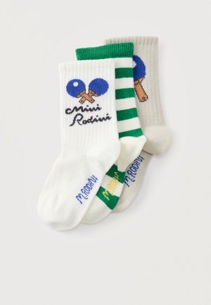 Trzy pary dziecięcych skarpetek z niebieskimi rakietkami i piłeczkami do ping-ponga, zielonymi paskami i wzorami tekstowymi na białym i szarym tle.