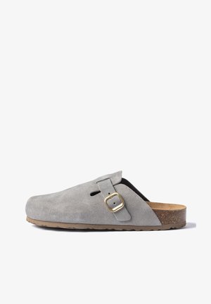 Zueco gris de ante sin cordones con una correa con hebilla dorada y una plantilla contorneada de corcho sobre una suela de goma texturizada.