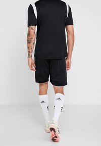 Musta urheilupaita, jossa valkoiset sivukoristeet, yhdistetty mustiin shortseihin. Valkoiset sukat ja nappulakengät, joissa on vaaleanpunaiset pohjat, täydentävät urheiluasun.