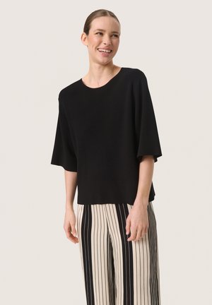 Black short-sleeve top with a relaxed fit and a round neckline, paired with high-waisted striped pants in black and white.
