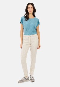 Lichtblauw shirt met korte mouwen en een textuurpatroon, gecombineerd met crèmekleurige joggerpants met zakken en een trekkoord. Grijze sportschoenen.