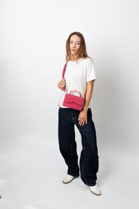 Ung kvinna i vit skjorta, mörka vida jeans och vita sneakers som håller en röd handväska �över axeln mot en plain vit bakgrund.