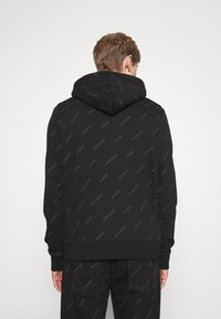 Sudadera negra con un patrón de logo que presenta el texto "SANDRO PARIS". Confeccionada con tejido suave, cuenta con capucha con cordón y puños de canalé.