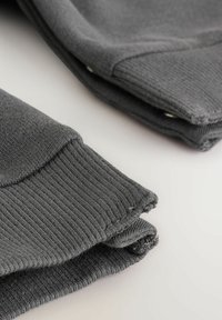Graues, geripptes Strickgewebe mit gefaltetem Design. Sichtbare Nähte und Stoffstruktur; glatte Oberfläche und weiches Erscheinungsbild. Akzente von Stichdetails.