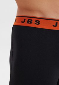 Zwarte katoenen boxershorts met een oranje tailleband waarop "JBS" in het zwart is gedrukt. Glad textuur, aansluitend ontwerp.