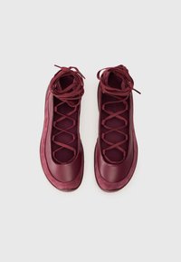 Burgundy sportskor med stängd design, texturerade överlägg och korsettsnörning. Syntetmaterial i mocka och mesh ger en distinkt look.