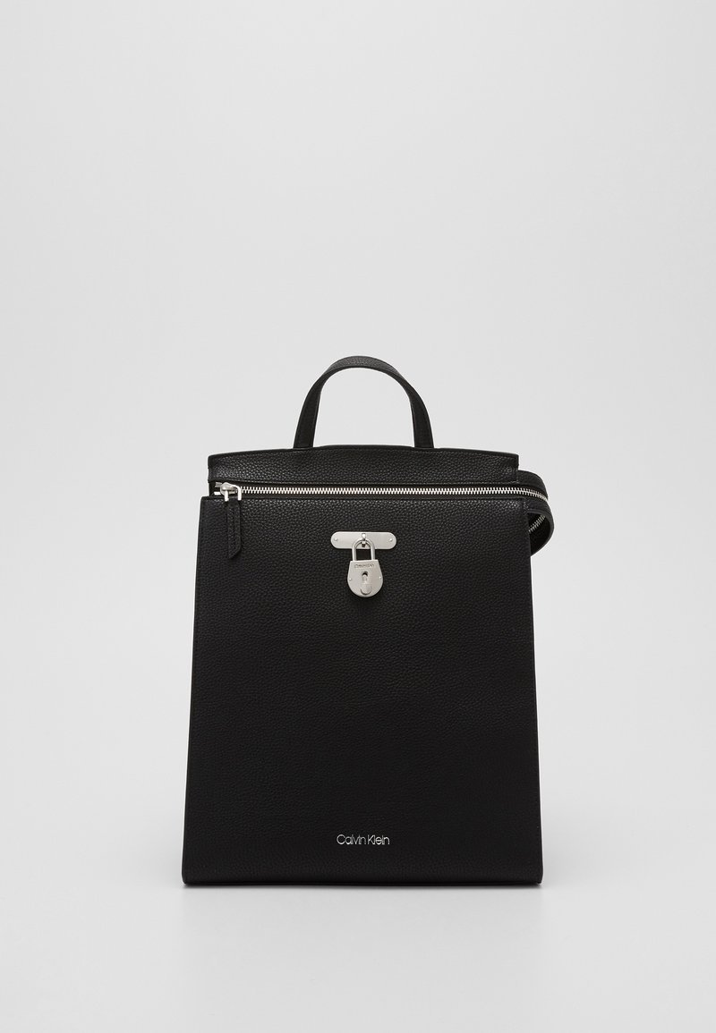 Sac à main Calvin Klein noir avec poignée supérieure, fermeture éclair argentée et détail de serrure avant en argent sur fond uni.