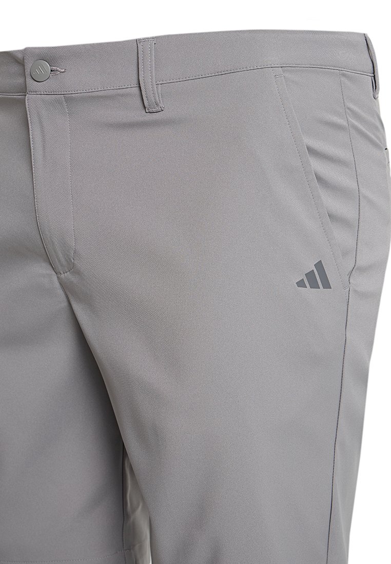 Pantalones deportivos grises con una textura suave, bolsillos laterales en ángulo y un emblema de logo discreto en el muslo izquierdo.