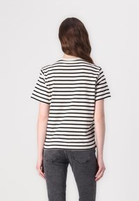 Tricou scurt cu mânecă în dungi, de culoare crem cu dungi orizontale negre, având un guler clasic și o croială lejeră. Vizibil din spate.