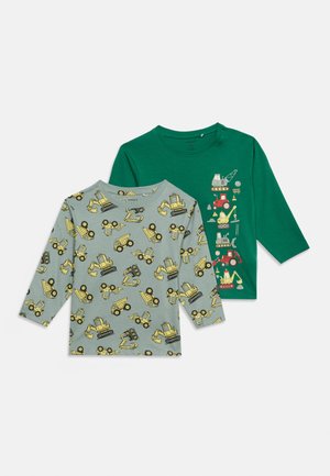 Deux chemises à manches longues pour enfants : une grise avec un motif de véhicules de chantier jaunes, une verte avec des illustrations verticales de véhicules de chantier.