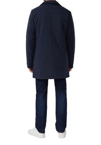 Marineblauwe lange jas met een rechte snit, voorzien van een kraag en een gladde textuur, gecombineerd met donkere jeans en witte sneakers.