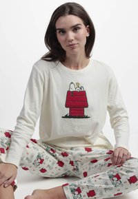 Top de manga larga crema con bordado de Snoopy y Woodstock. Los pantalones de pijama a juego presentan un colorido patrón de dibujos animados y un corte relajado.