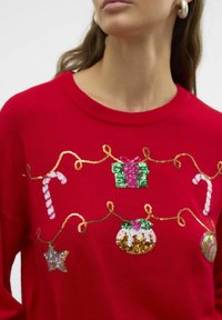 Maglione rosso lavorato a maglia con ricami festivi, tra cui bastoncini di zucchero, regali e ornamenti in paillettes e filo metallico.