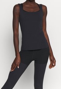 Débardeur noir sans manches avec un col carré, fabriqué en tissu lisse. Associé à des leggings noirs texturés au design ajusté.