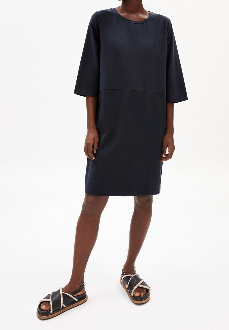 Granatowa sukienka bawełniana z okrągłym dekoltem, rękawami o długości trzech ćwierci i prostym krojem. Połączona z czarnymi sandałami z białymi akcentami ze sznurka.