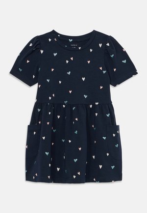 Dunkelblaues Kleid mit kurzen Puffärmeln, ausgestattet mit einem gerafften Rock und Taschen. Verziert mit mehrfarbigen Herzmustern in Rosa und Türkis.