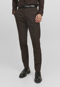 Pantaloni a quadri marroni con vestibilità su misura, caratterizzati da una texture liscia, passanti per la cintura e tasche laterali. Abbinati a mocassini neri.
