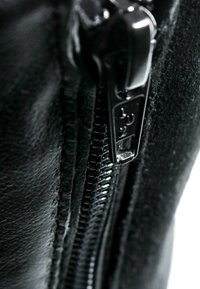Gros plan d'un curseur de fermeture éclair noir glissant le long des dents du zip sur un tissu noir, montrant la texture et les détails de couture.